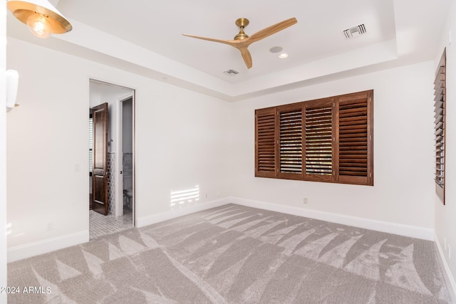 carpeted spare room featuring a raised ceiling and ceiling fan