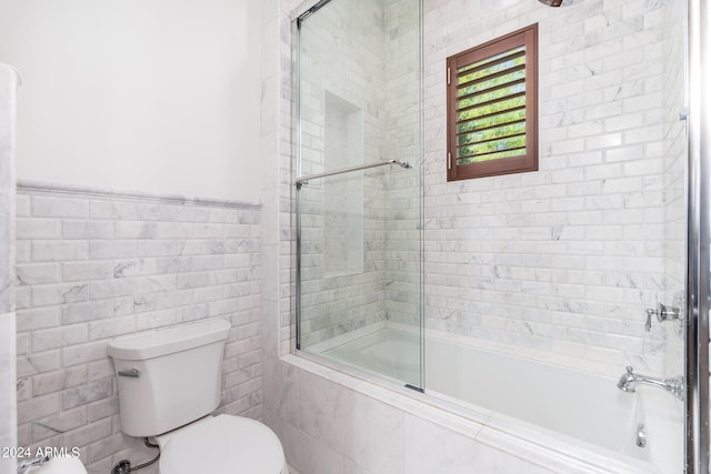 bathroom featuring tile walls, enclosed tub / shower combo, and toilet