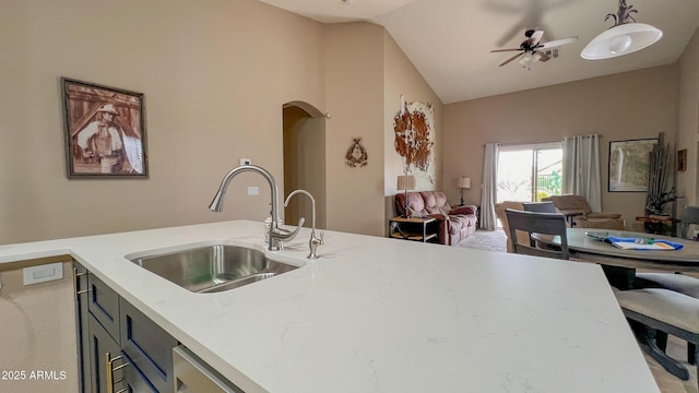 kitchen featuring light stone countertops, open floor plan, vaulted ceiling, arched walkways, and a sink