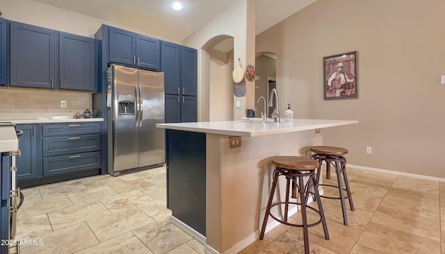 kitchen with a breakfast bar area, decorative backsplash, stainless steel refrigerator with ice dispenser, arched walkways, and blue cabinets