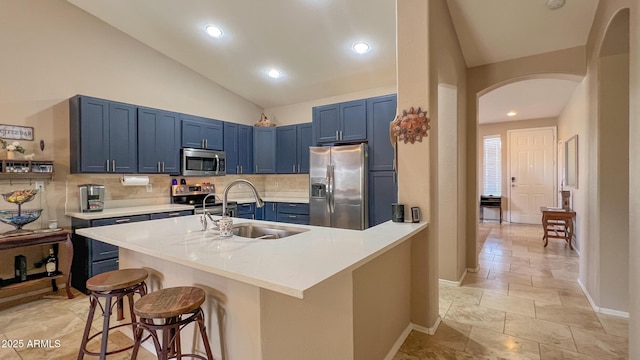 kitchen with blue cabinetry, arched walkways, a sink, appliances with stainless steel finishes, and a kitchen bar