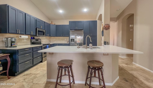 kitchen with blue cabinetry, decorative backsplash, appliances with stainless steel finishes, and a breakfast bar area