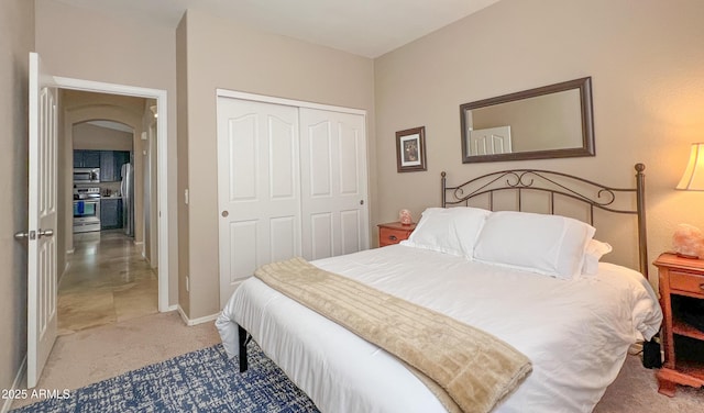 bedroom with baseboards, light colored carpet, arched walkways, freestanding refrigerator, and a closet