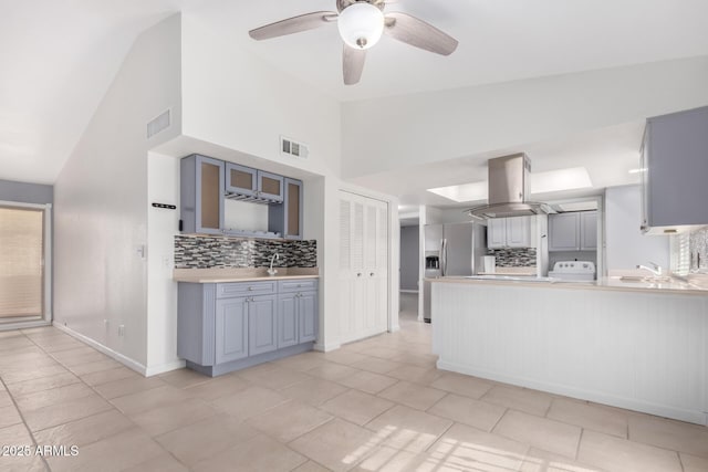 kitchen with island exhaust hood, stainless steel refrigerator with ice dispenser, tasteful backsplash, and gray cabinetry