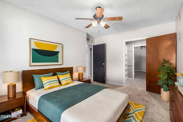 bedroom with a closet, a textured ceiling, ceiling fan, a walk in closet, and light carpet