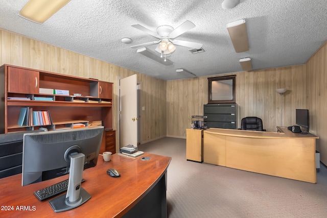 carpeted office with wood walls, ceiling fan, and a textured ceiling