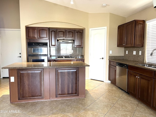 kitchen featuring tasteful backsplash, a kitchen island, sink, appliances with stainless steel finishes, and light tile patterned floors