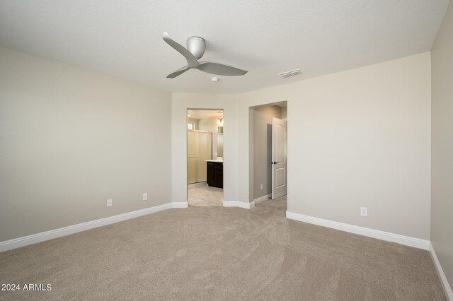 unfurnished bedroom featuring light colored carpet, ensuite bathroom, and ceiling fan