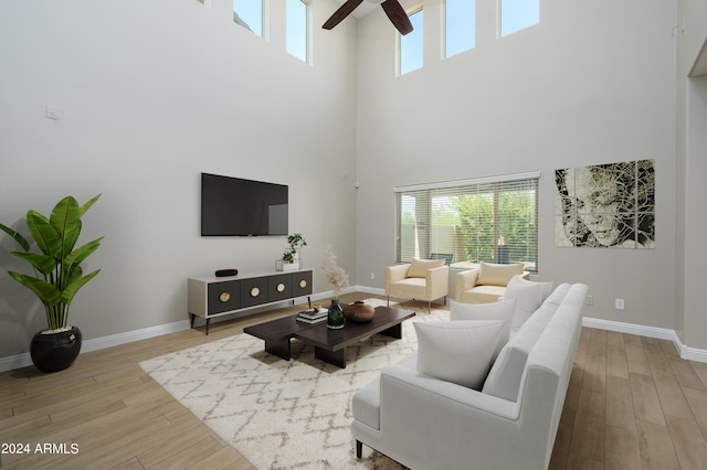 living room featuring ceiling fan, light hardwood / wood-style floors, and a high ceiling