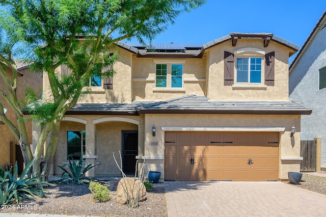 view of front of house featuring covered porch, stucco siding, roof mounted solar panels, decorative driveway, and a garage