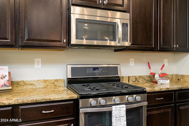 kitchen featuring stainless steel appliances, light stone counters, and dark brown cabinetry