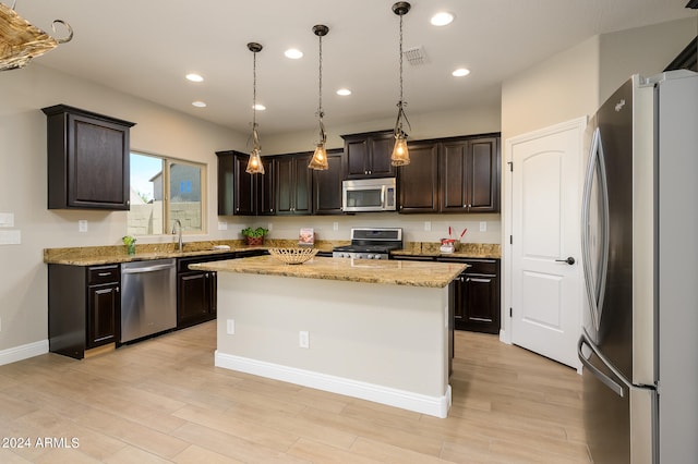 kitchen with appliances with stainless steel finishes, light stone counters, a kitchen island, and dark brown cabinets