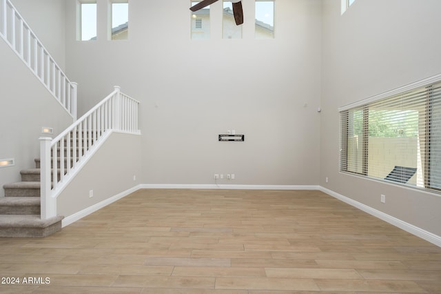 interior space featuring stairs, baseboards, a high ceiling, light wood finished floors, and ceiling fan