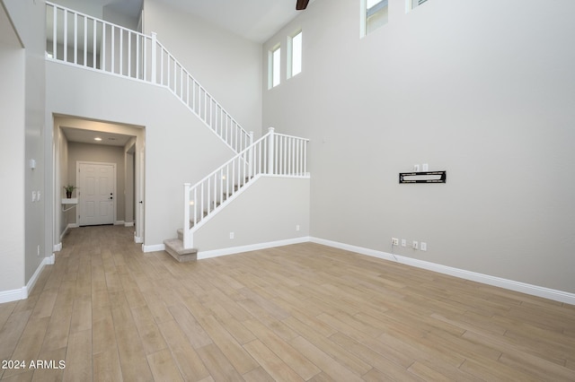 unfurnished living room with light wood finished floors, baseboards, a high ceiling, and stairway
