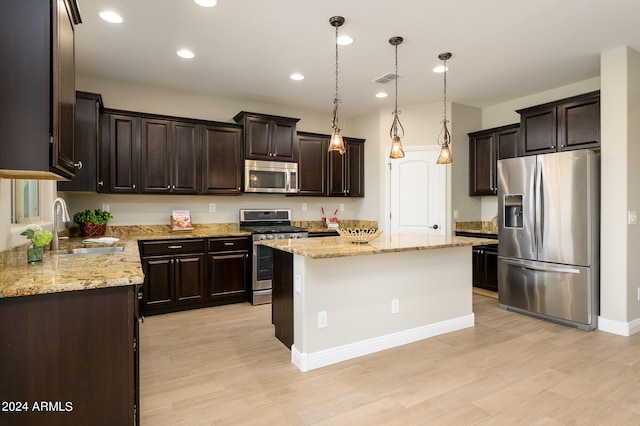 kitchen with appliances with stainless steel finishes, light hardwood / wood-style flooring, sink, light stone countertops, and a kitchen island