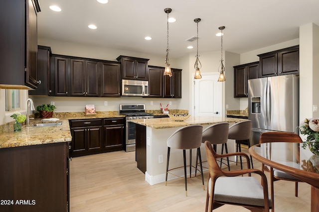 kitchen with a breakfast bar, a kitchen island, appliances with stainless steel finishes, dark brown cabinetry, and a sink