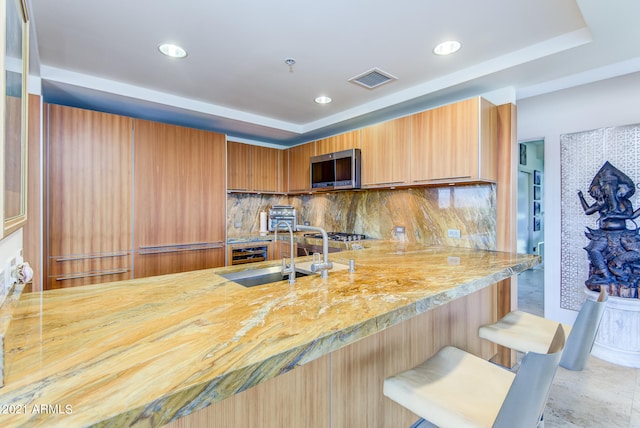 kitchen with a kitchen breakfast bar, decorative backsplash, a raised ceiling, kitchen peninsula, and sink