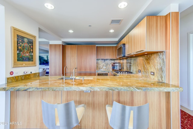 kitchen featuring sink, kitchen peninsula, a kitchen bar, backsplash, and appliances with stainless steel finishes