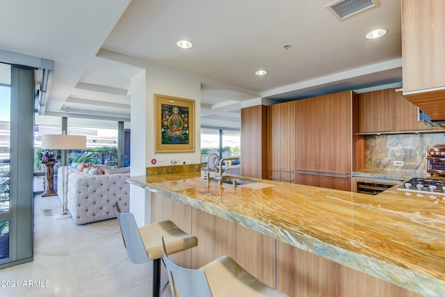 kitchen featuring a breakfast bar area, backsplash, kitchen peninsula, and sink