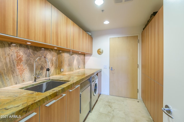 kitchen featuring light stone countertops, washer / clothes dryer, decorative backsplash, and sink