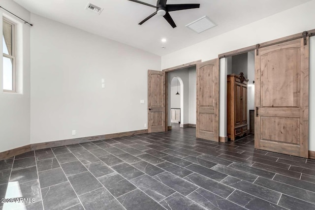 2009 S Raindance Rd, Apache Junction, AZ 85119 - unfurnished bedroom with a barn door, arched walkways, and ceiling fan