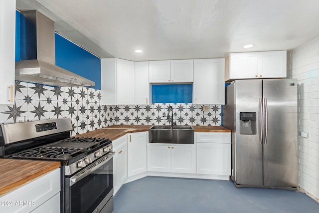 kitchen with butcher block counters, stainless steel appliances, wall chimney range hood, and backsplash