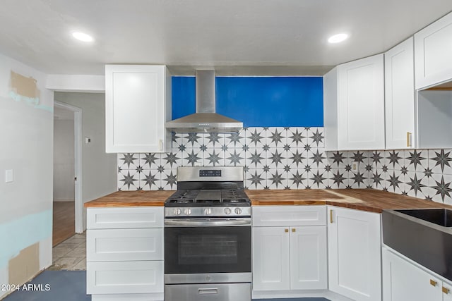 kitchen with decorative backsplash, wall chimney range hood, stainless steel gas range, white cabinets, and butcher block countertops