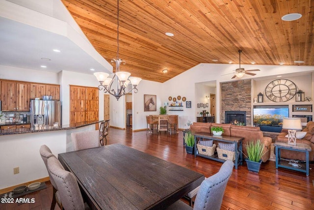 dining room with ceiling fan with notable chandelier, a stone fireplace, dark hardwood / wood-style floors, and wooden ceiling