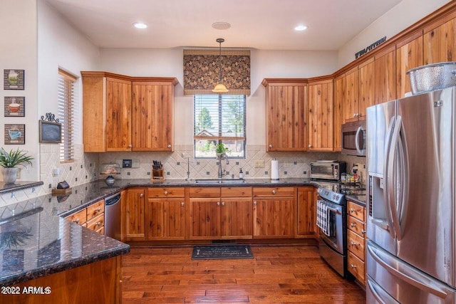 kitchen featuring decorative light fixtures, dark wood-type flooring, appliances with stainless steel finishes, sink, and tasteful backsplash