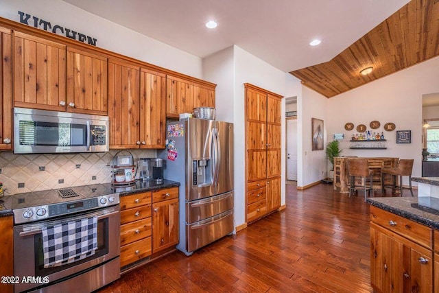 kitchen featuring tasteful backsplash, dark hardwood / wood-style flooring, lofted ceiling, stainless steel appliances, and dark stone countertops