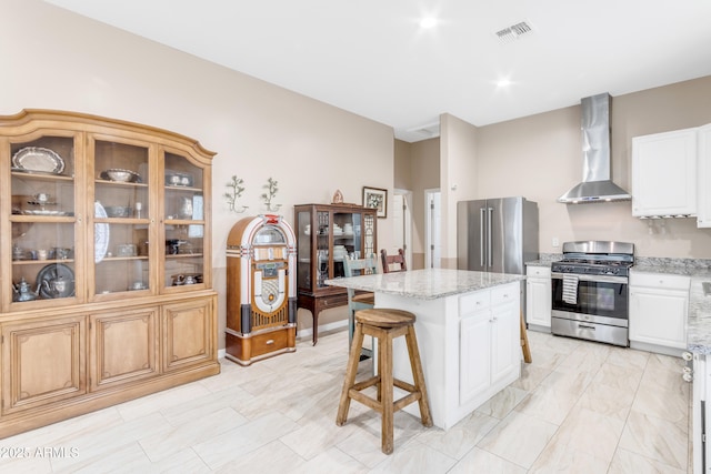 kitchen with white cabinets, appliances with stainless steel finishes, a kitchen island, and wall chimney range hood