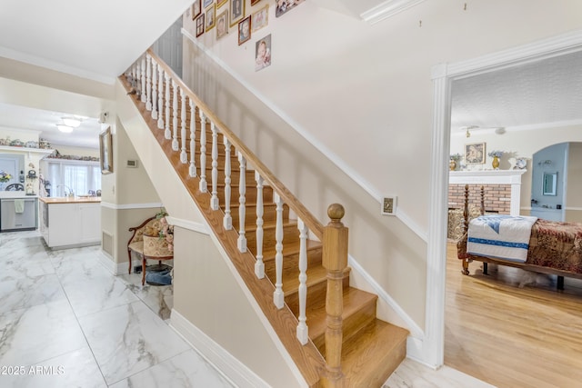 staircase with sink, ornamental molding, and a brick fireplace