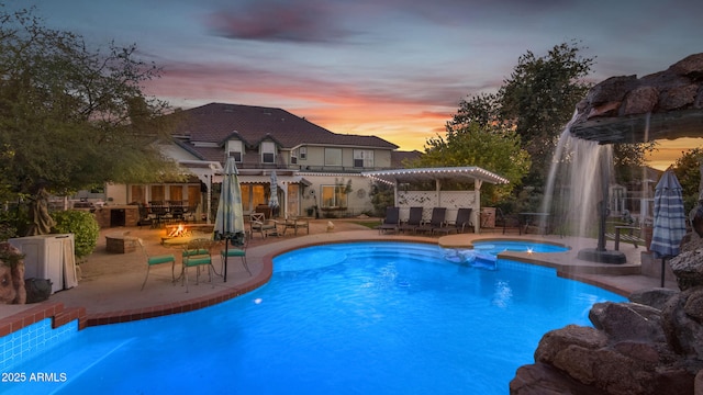 pool at dusk featuring a fire pit, a pergola, a patio, a bar, and an in ground hot tub