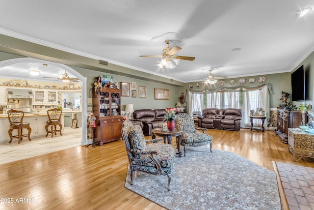 living room with ceiling fan, ornamental molding, and light hardwood / wood-style flooring