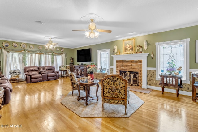 living room featuring a fireplace, light hardwood / wood-style flooring, ornamental molding, and ceiling fan