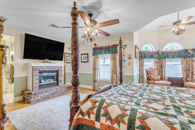 bedroom with a brick fireplace, light hardwood / wood-style flooring, ceiling fan, and ensuite bathroom