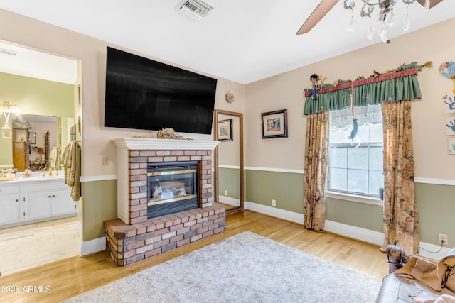 living room featuring ceiling fan, a brick fireplace, and light hardwood / wood-style flooring