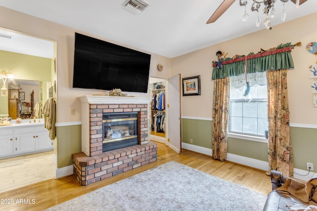 living room with a fireplace, ceiling fan, and light wood-type flooring