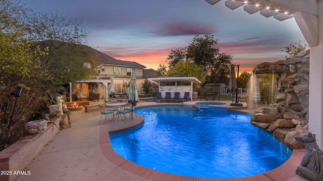 pool at dusk with an in ground hot tub, exterior bar, and a patio area