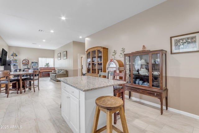 kitchen featuring a kitchen island, white cabinetry, light stone countertops, and a breakfast bar area