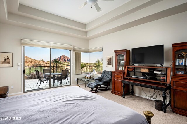 carpeted bedroom with ceiling fan, a tray ceiling, access to exterior, and multiple windows