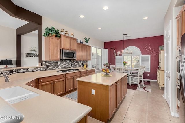 kitchen with sink, appliances with stainless steel finishes, hanging light fixtures, backsplash, and a center island