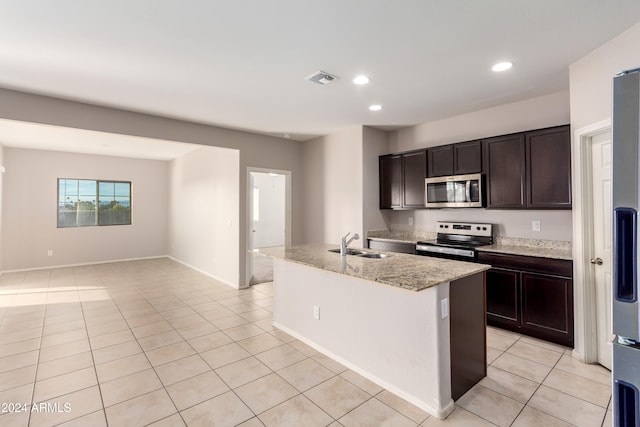 kitchen with stainless steel appliances, sink, light stone counters, dark brown cabinets, and a kitchen island with sink