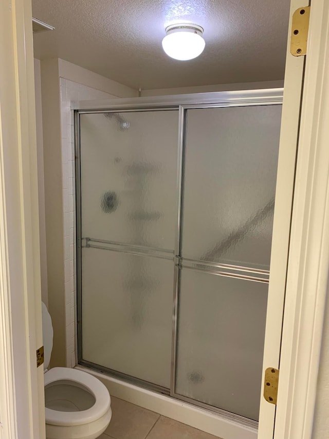 bathroom with a textured ceiling, a shower with door, tile patterned floors, and toilet