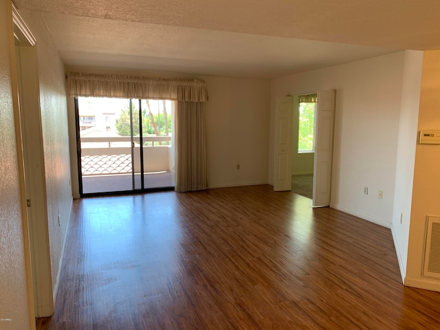 spare room featuring a textured ceiling, dark hardwood / wood-style floors, and a healthy amount of sunlight