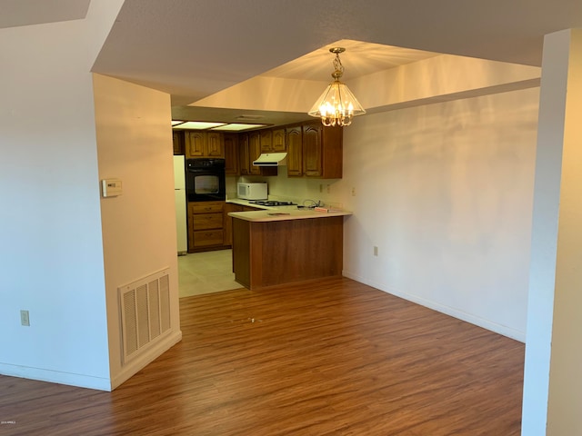 kitchen featuring white appliances, kitchen peninsula, pendant lighting, an inviting chandelier, and light hardwood / wood-style flooring