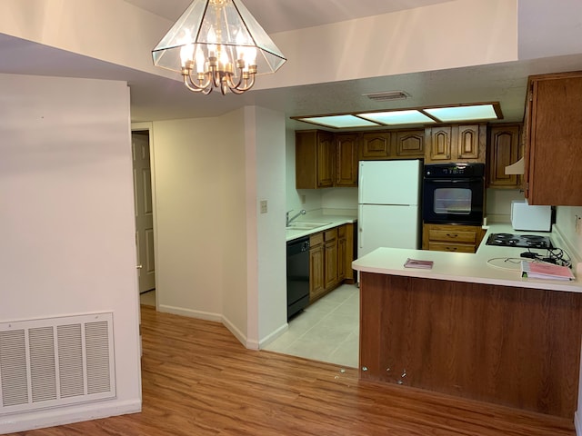 kitchen with a notable chandelier, kitchen peninsula, hanging light fixtures, light hardwood / wood-style flooring, and black appliances