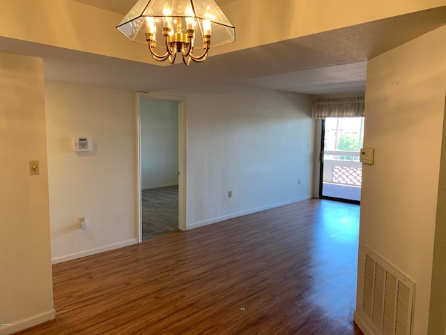 empty room featuring a chandelier, a textured ceiling, and dark wood-type flooring