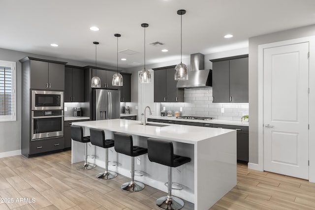 kitchen with wall chimney exhaust hood, a breakfast bar, stainless steel appliances, light countertops, and a sink