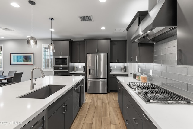 kitchen featuring visible vents, wall chimney exhaust hood, stainless steel appliances, light countertops, and a sink